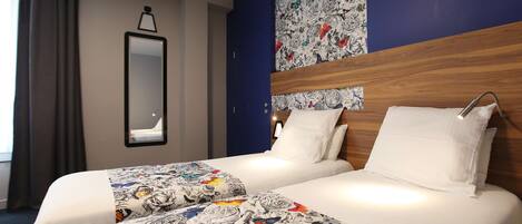 Habitación de hotel con dos camas, un espejo grande y un papel tapiz estampado con flores.