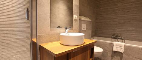 A modern bathroom with a wooden vanity, a white sink, a mirror, a toilet, and a bathtub.