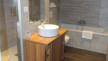 A modern bathroom with a wooden vanity, a white sink, a glass shower enclosure, and a bathtub.