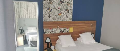 A hotel room with a bed, a bedside table with a lamp, a mirror, and a floral-patterned wall.