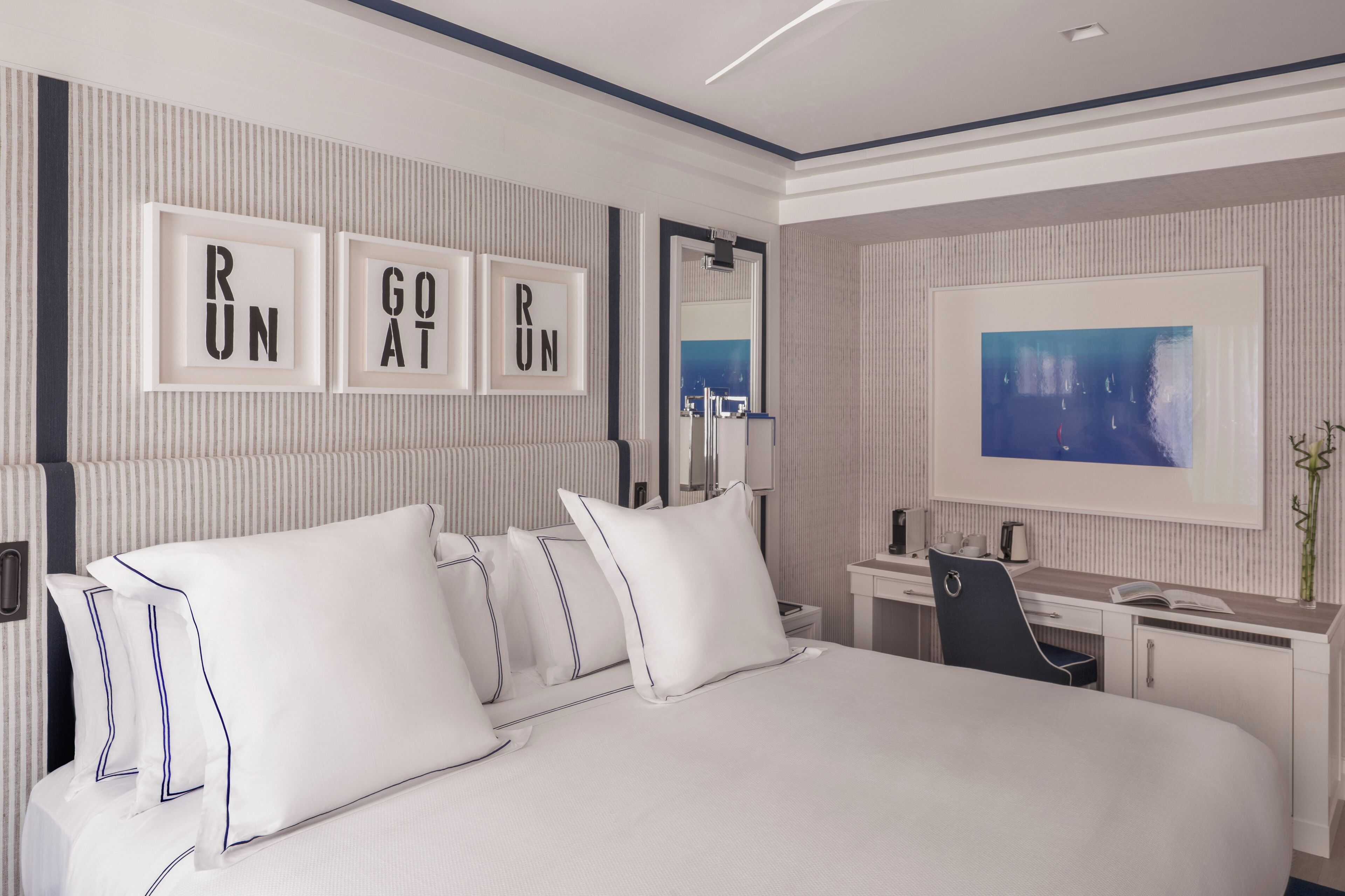 Una habitación de hotel moderna con una cama grande, un escritorio y una silla. Hay cuadros en la pared y un cuadro sobre el escritorio.