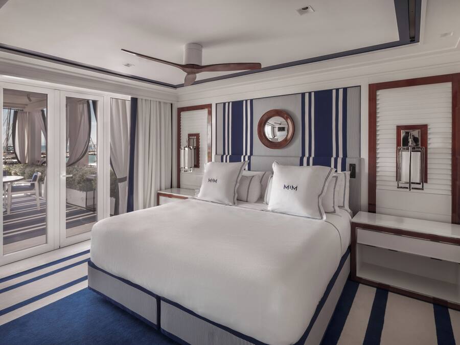 Quarto de hotel com cama grande, ventilador de teto, vista para a praia e chão listrado.