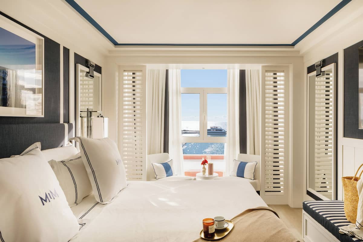 A hotel room with a large bed, a view of the city, and a balcony with a railing.