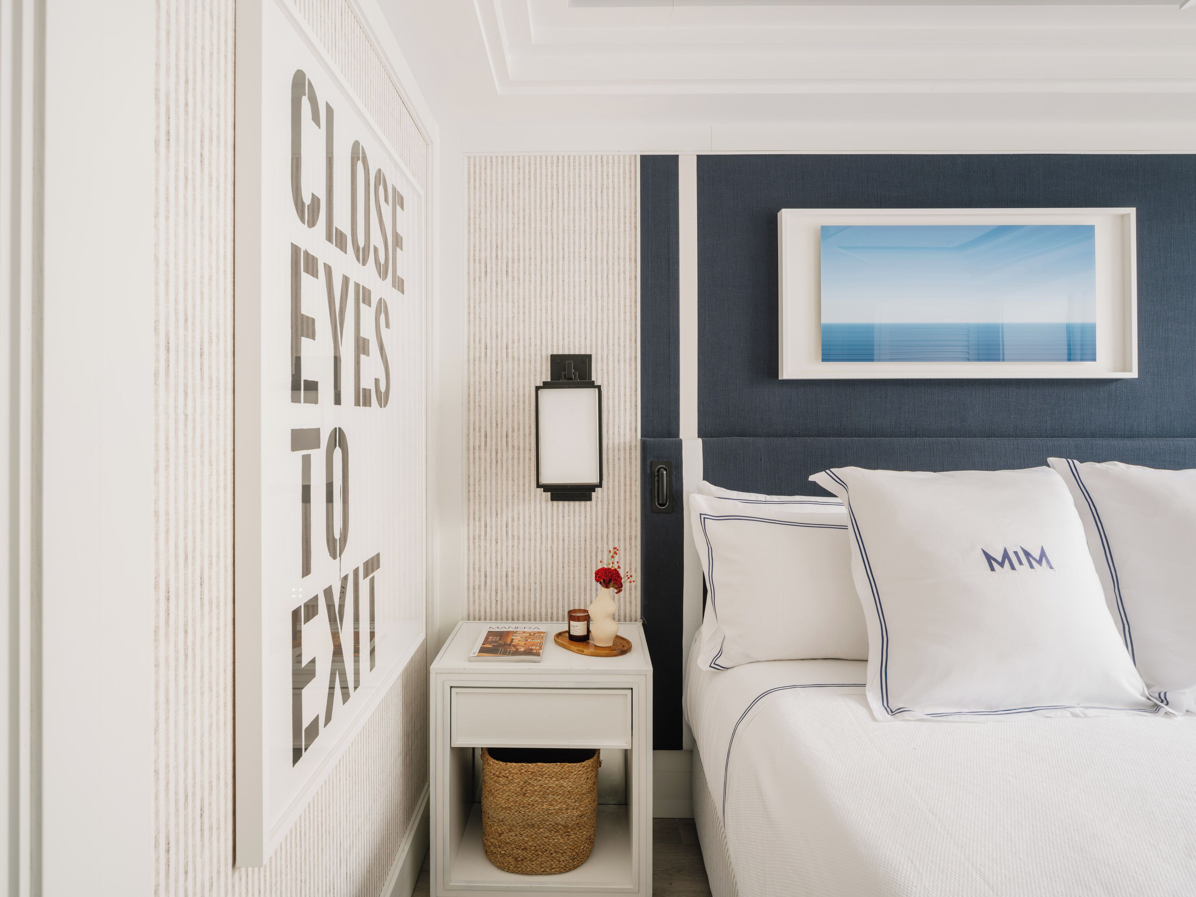 Un dormitorio con cama, mesita de noche, lámpara de pared, un cuadro enmarcado y un letrero decorativo.