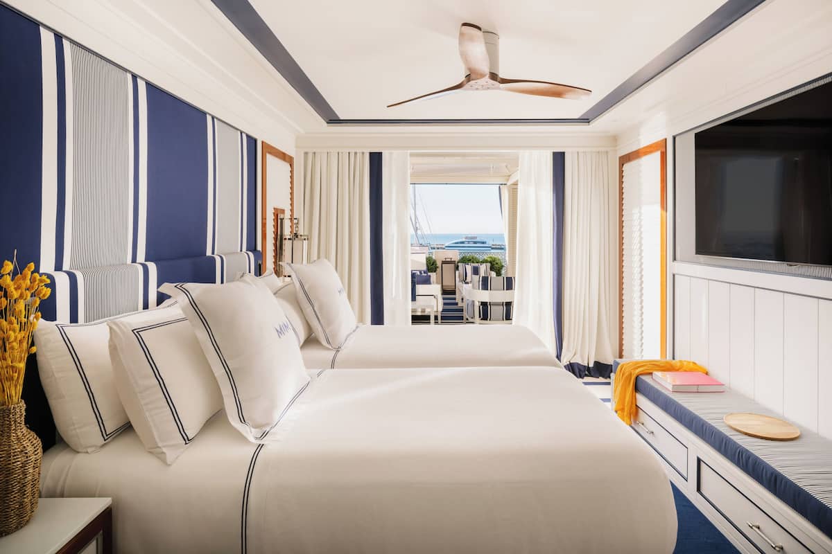 A hotel room with a large bed, a TV, a balcony with a view, and a ceiling fan.