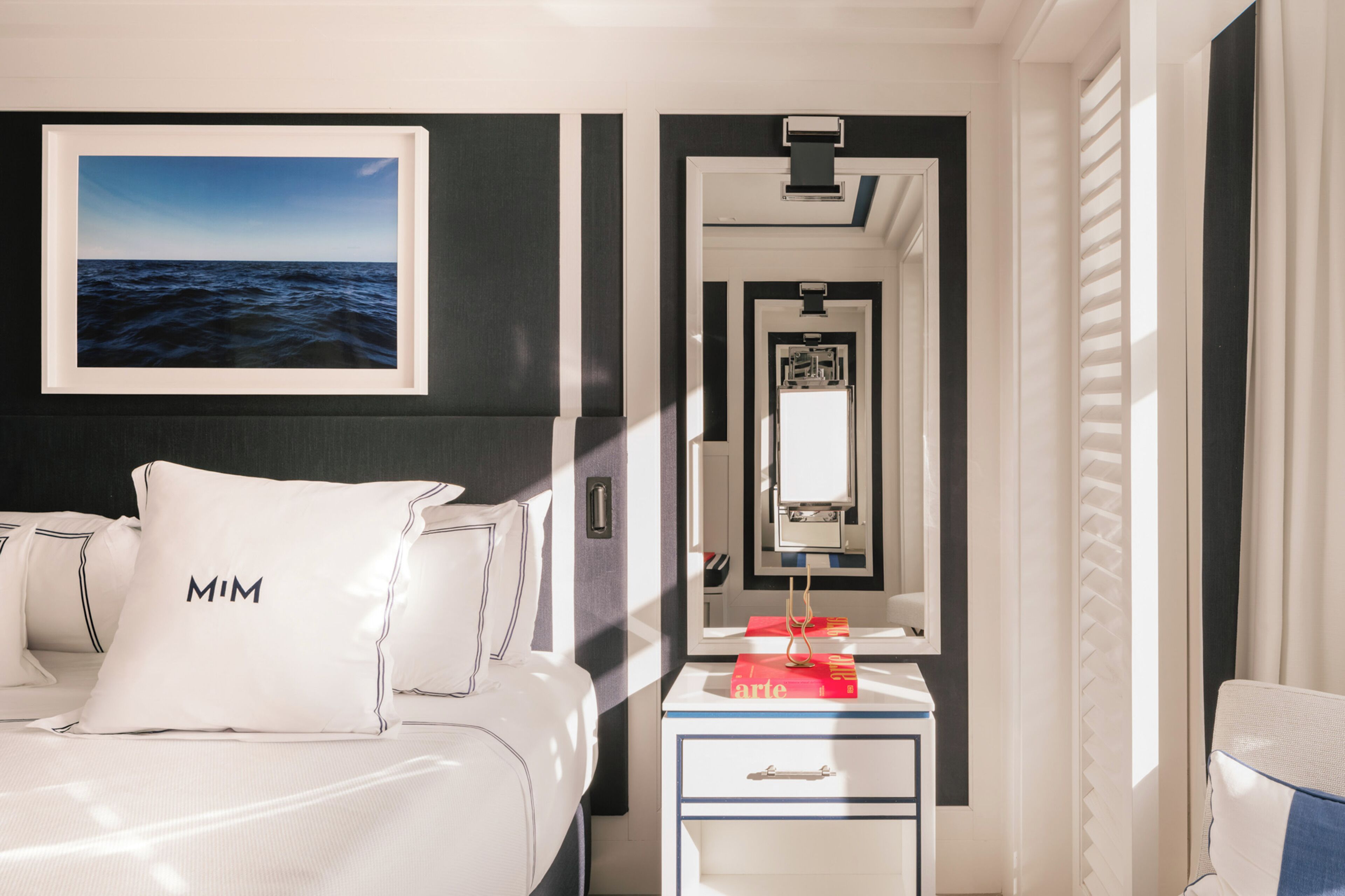 A hotel room with a bed, a nightstand, a mirror, and a framed picture of the ocean.