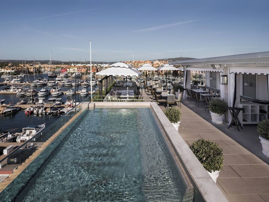 Une piscine sur le toit offrant une vue sur le port de plaisance, des espaces de détente en plein air et des plantes en pot.