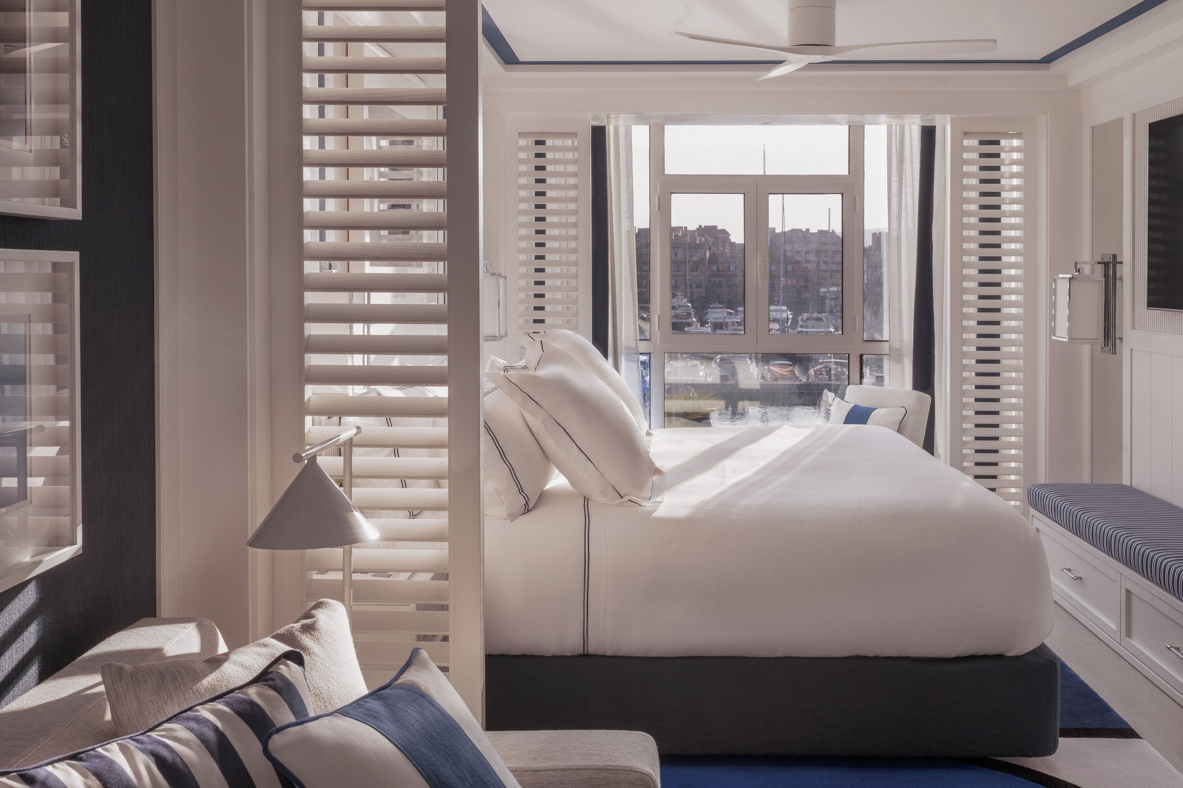 A bedroom with a large bed, a bedside table, a lamp, and a view of the city through the window.