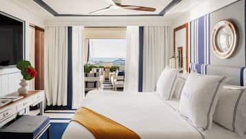 Habitación de hotel con una cama grande, un escritorio con computadora, televisión y vista al océano.