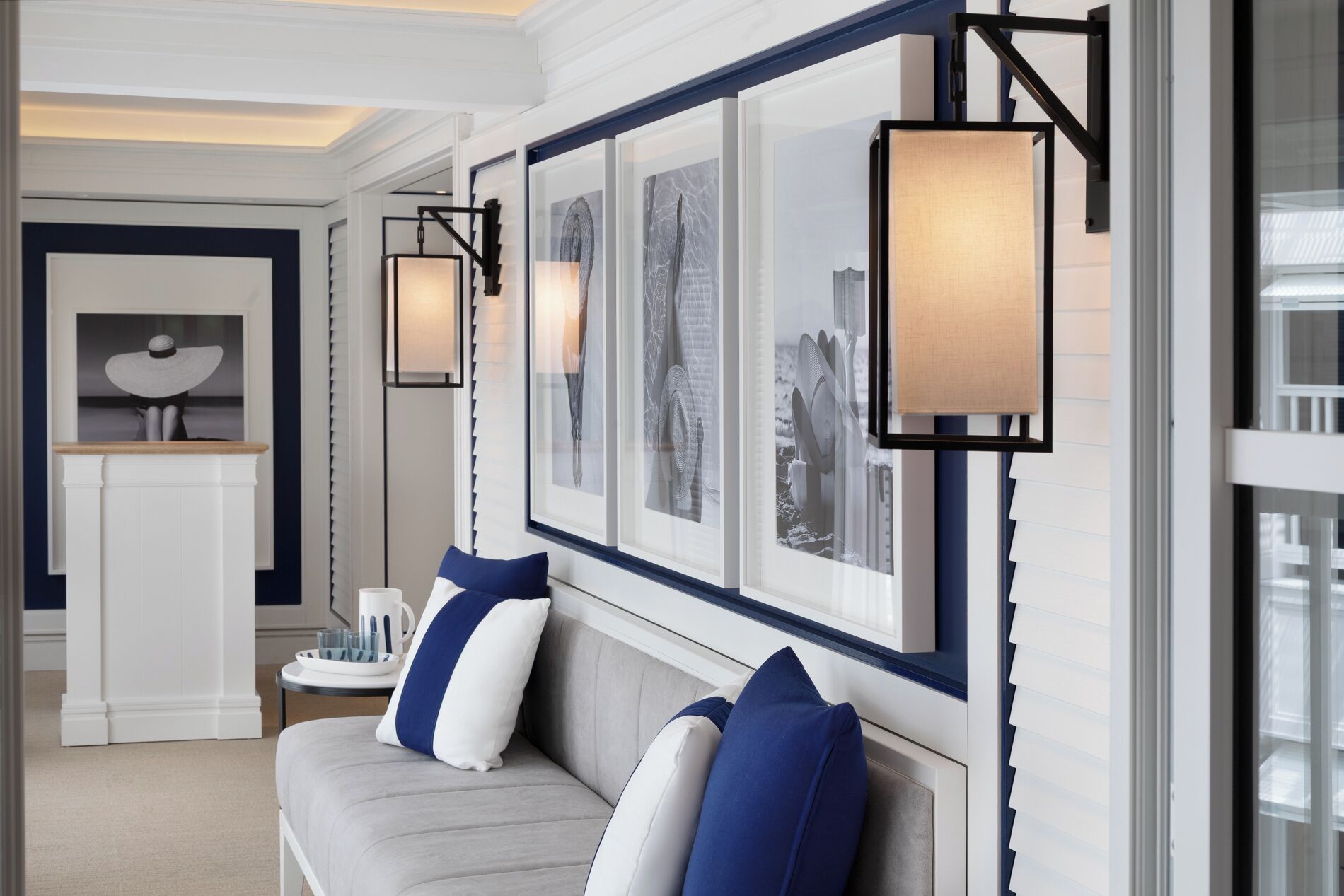 Quarto de hotel moderno com sofá cinza, almofadas azuis e brancas e obras de arte emolduradas na parede.
