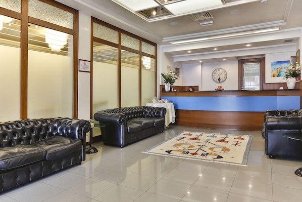 A hotel lobby with leather sofas, a reception desk, and a decorative rug. - Sunset (Rimini)