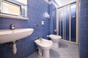 A bathroom with a sink, bidet, toilet, and a shower area. - Sunset (Rimini)
