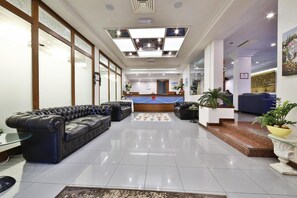 A spacious lobby with a reception desk, leather sofas, and a tiled floor. - Sunset (Rimini)