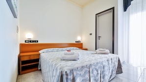 Ett hotellrum med en säng, sängbord, en garderob och en dörr.