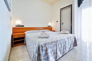A hotel room with a bed, bedside tables, a wardrobe, and a door. - Sunset (Rimini)