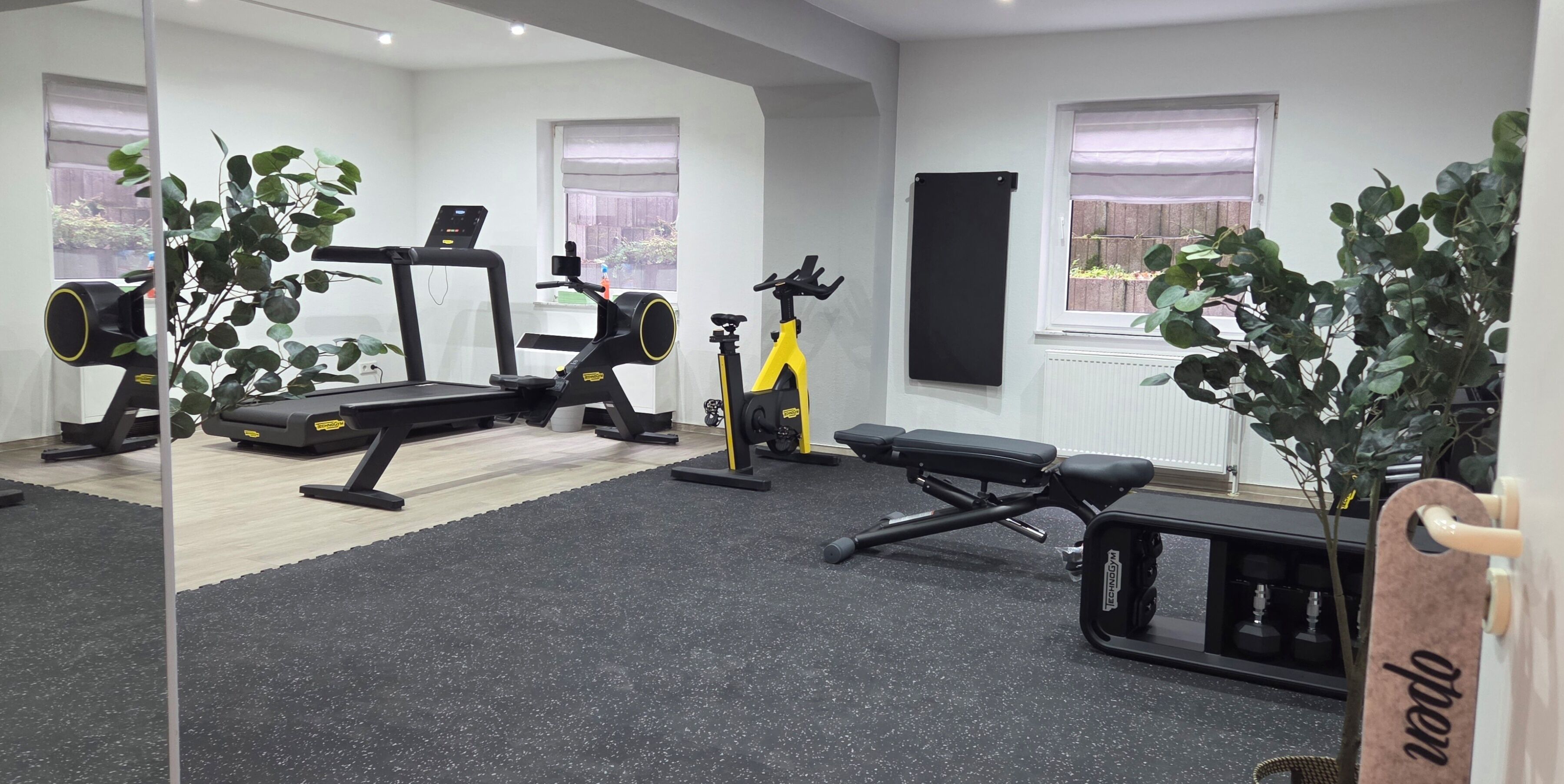 Une salle de sport à domicile équipée de matériel d’exercice, notamment un tapis de course, un vélo d’appartement et un banc de musculation.