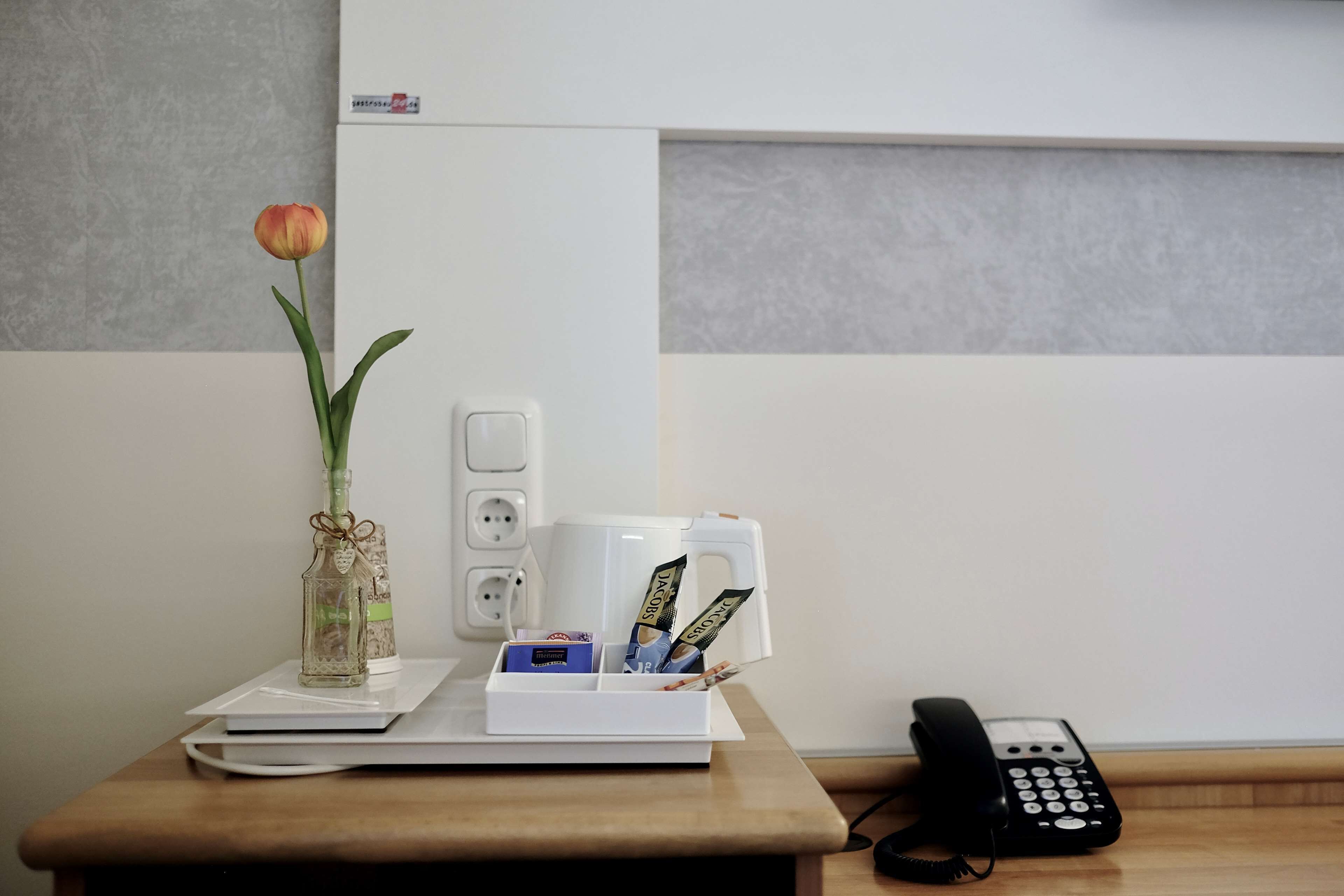 A desk with a vase of flowers, a coffee maker, a phone, and a box of tissues.