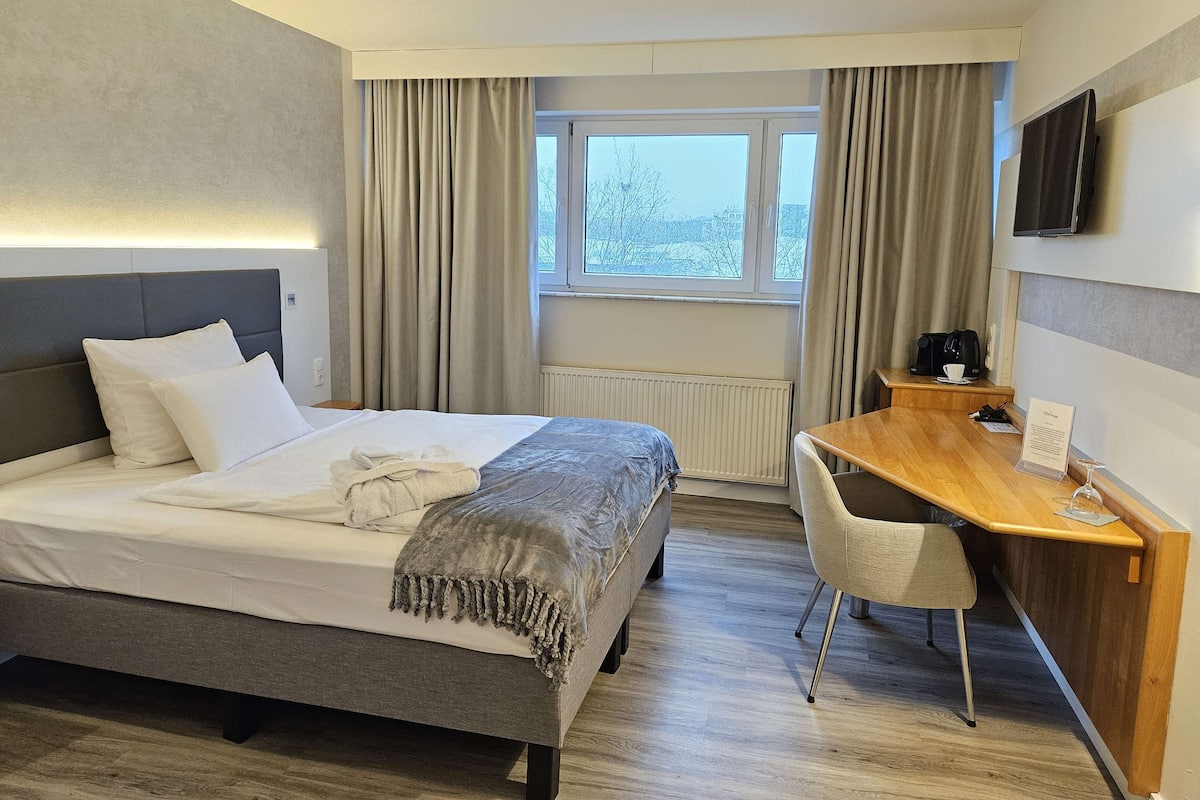 Hotelkamer met een bed, bureau, stoel, televisie en raam met gordijnen.