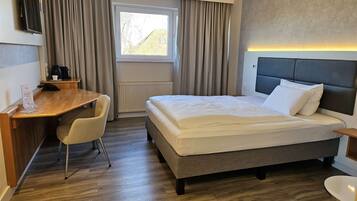 A hotel room with a bed, a desk, a chair, a television, and a window with curtains.