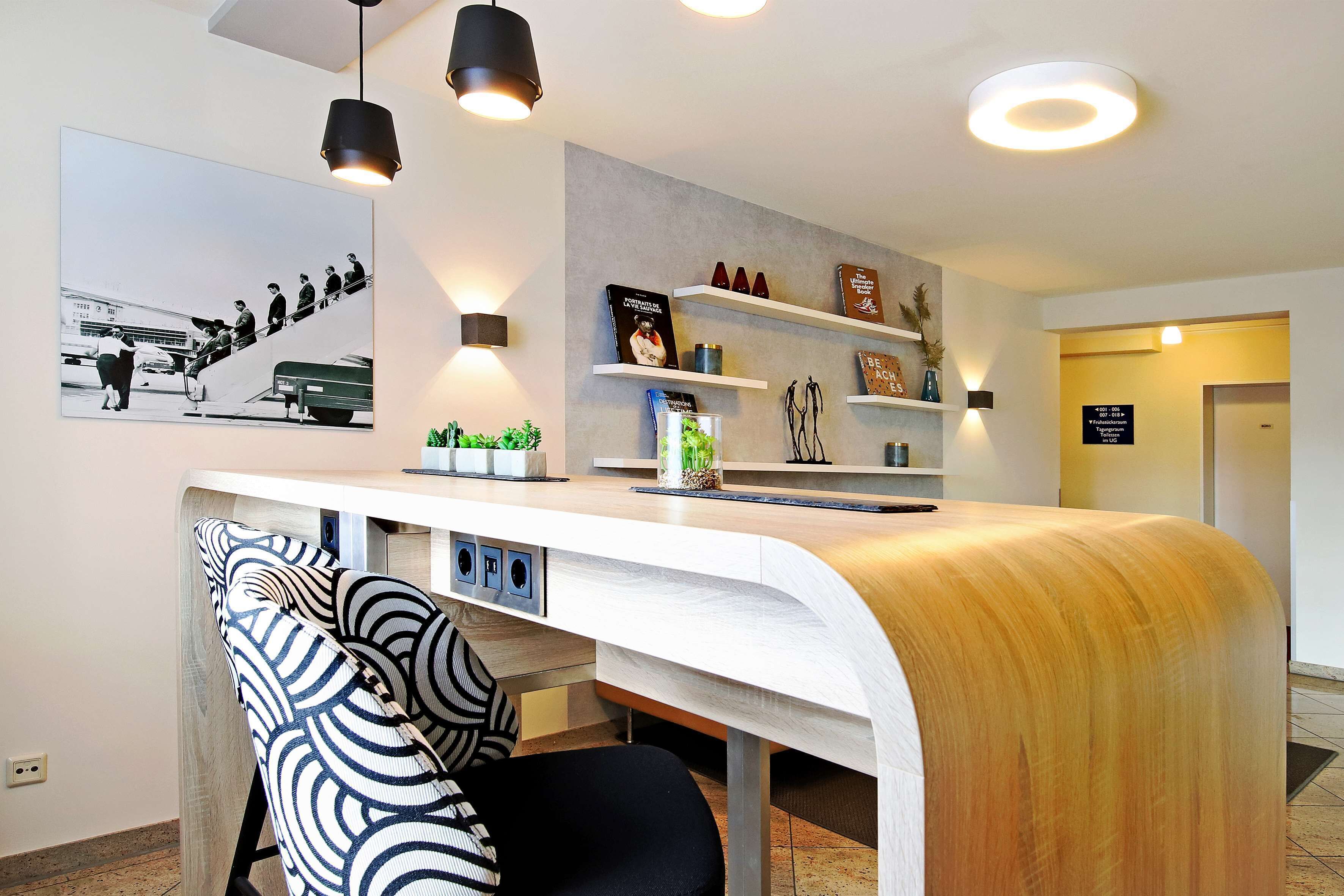 Een modern receptiebalie met een gebogen ontwerp, een stoel met zwart-wit patroon en een wandplank met decoratieve objecten.