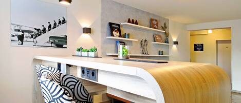 Een modern receptiebalie met een gebogen ontwerp, een stoel met zwart-wit patroon en een wandplank met decoratieve objecten.