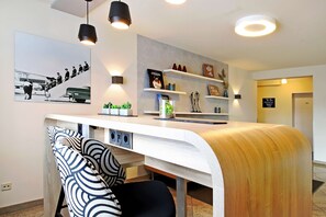 Un comptoir d’accueil moderne au design incurvé, une chaise à motifs noir et blanc et une étagère murale agrémentée d’objets décoratifs.
