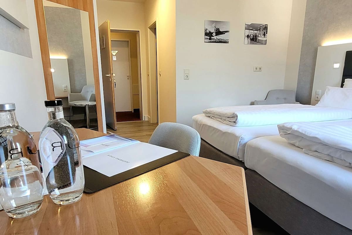 Een hotelkamer met een houten bureau, twee bedden, een spiegel en een deur naar een andere kamer.