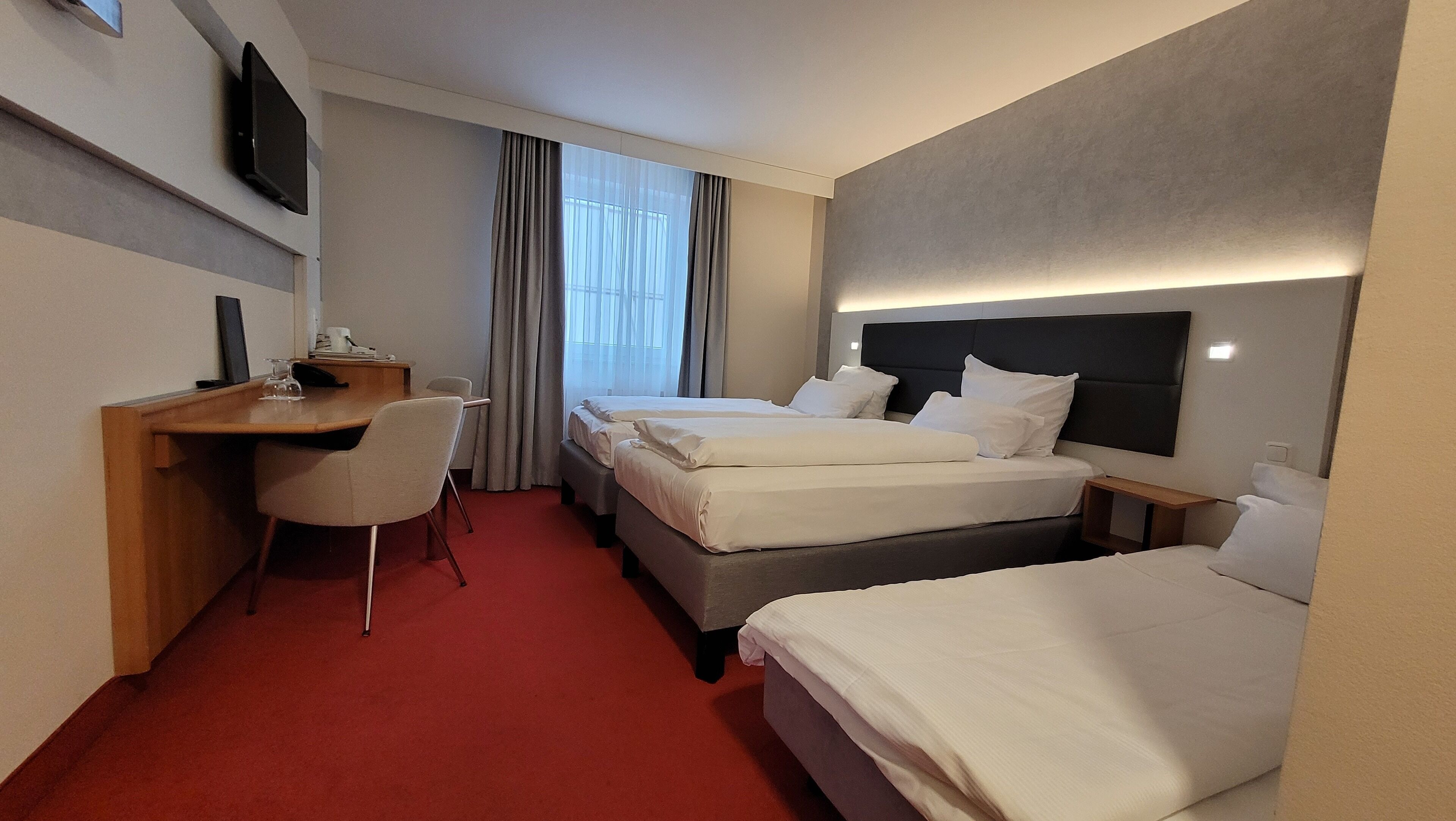 A hotel room with two beds, a desk, a chair, and a TV on the wall.