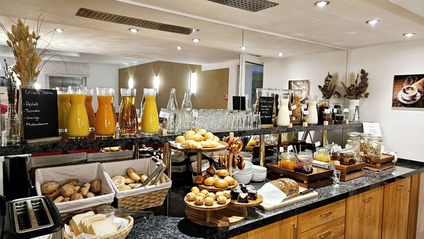 Un buffet proposant une variété de plats et de boissons, notamment du pain, des pâtisseries et un assortiment de jus de fruits.