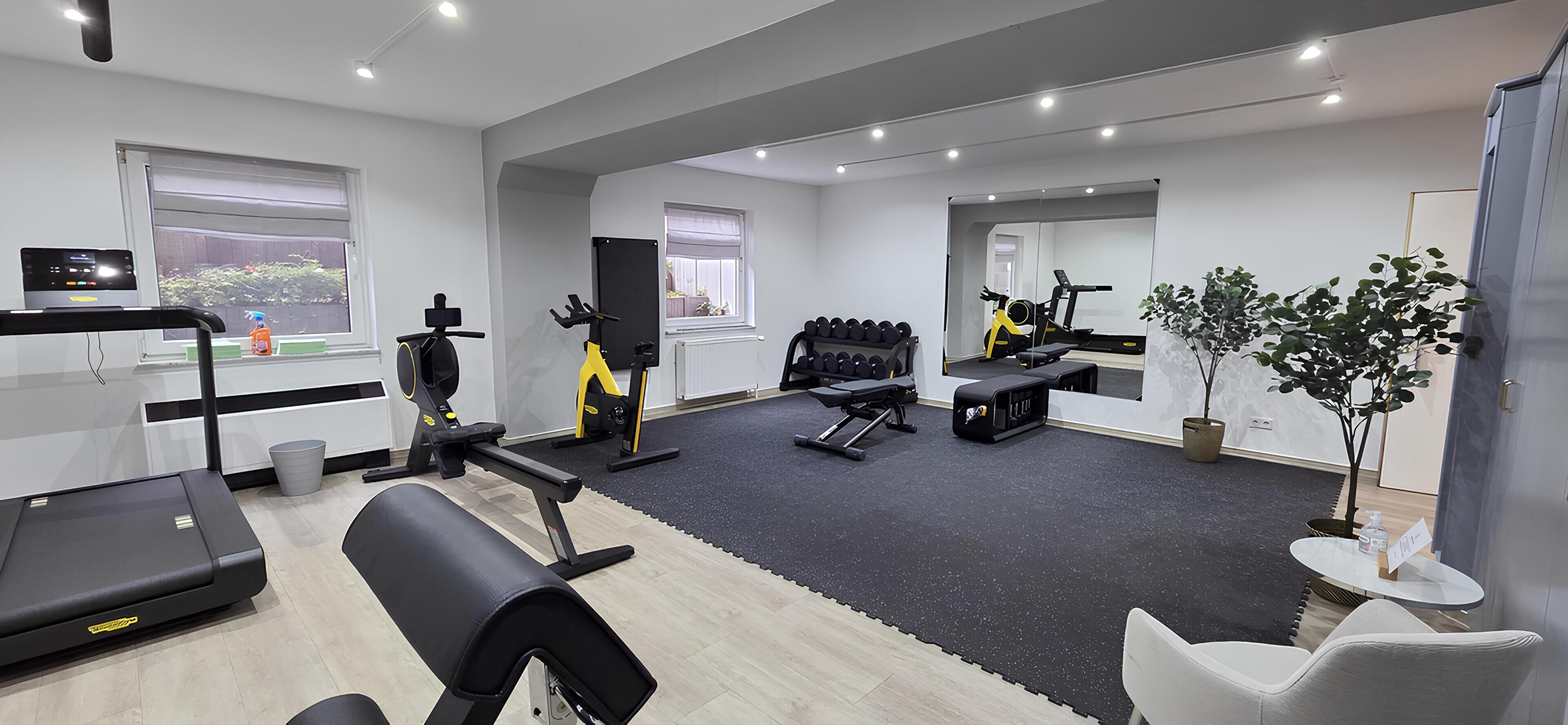 Ein modernes Fitnessstudio mit verschiedenen Trainingsgeräten, einem Laufband und einem Spiegel, der den Raum widerspiegelt.