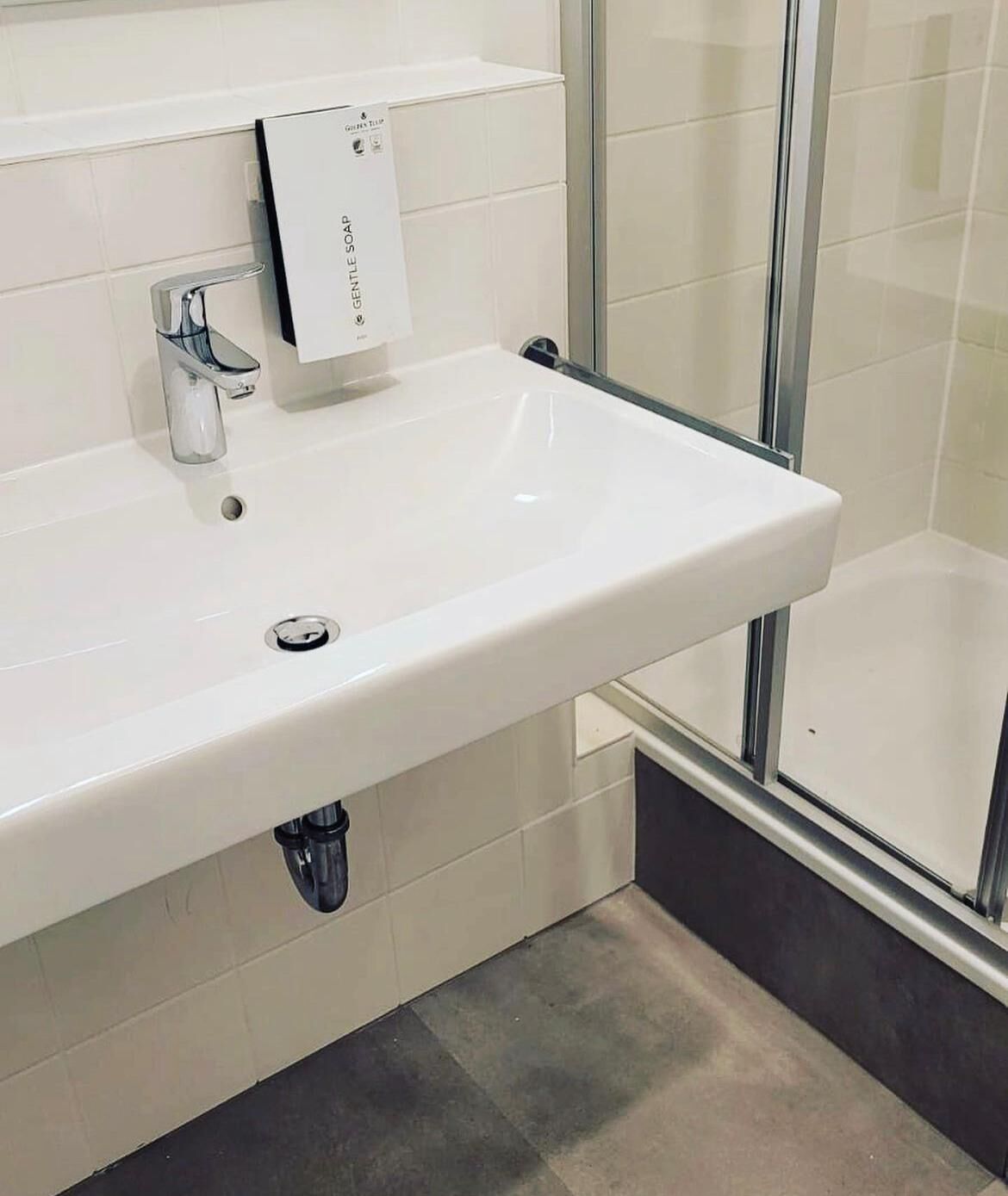 Un baño moderno con un lavamanos blanco, grifo cromado y cabina de ducha con mampara de vidrio.