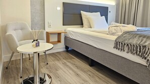 Une chambre d’hôtel moderne, équipée d’un lit, d’une petite table, d’une chaise et d’une table de chevet sur laquelle se trouve une bouteille d’eau.