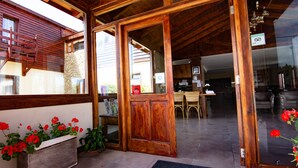 Ein Holzinterieur mit einer Rezeption, einem Essbereich und einer durch eine offene Tür einsehbarer Küche.