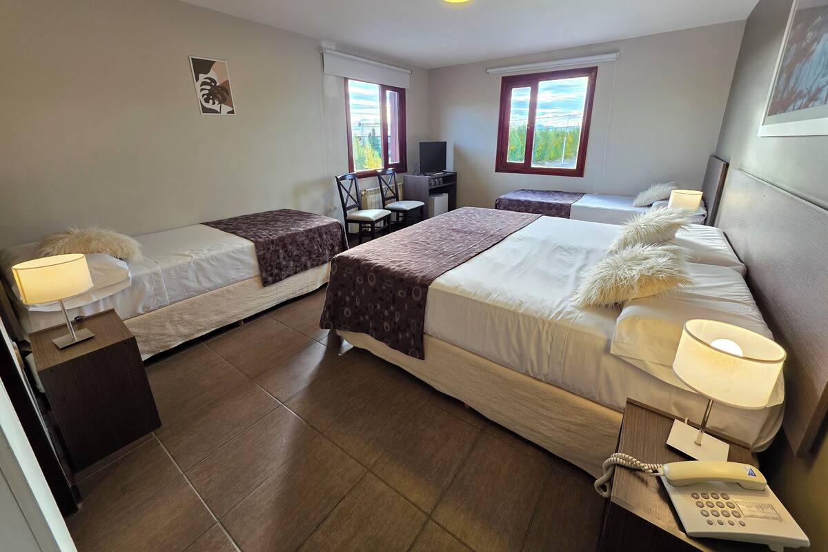 Une chambre d’hôtel avec deux lits simples, un bureau avec une chaise, une télévision et un téléphone.