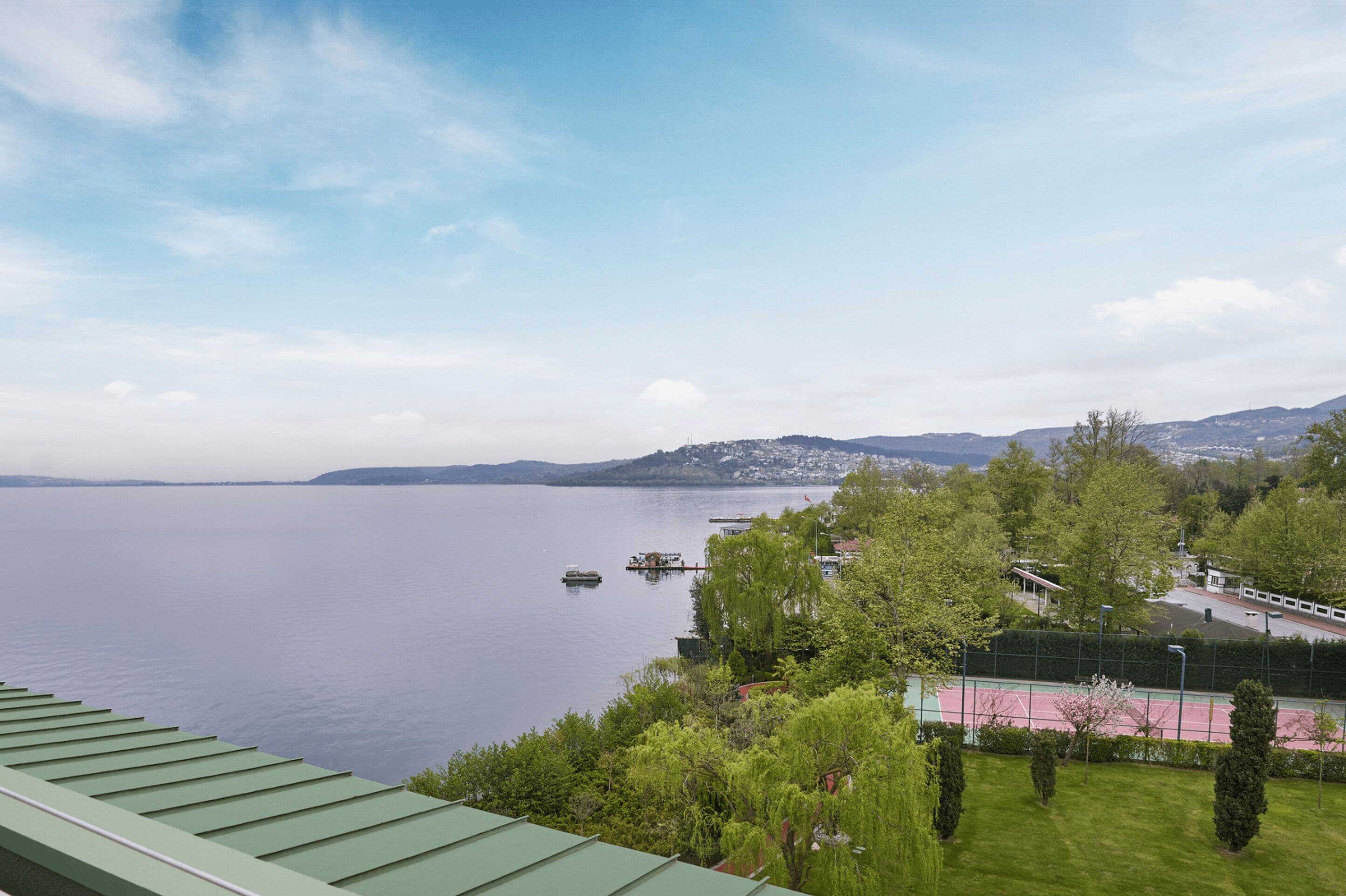 A view of a lake with boats, a tennis court, and a city in the distance.