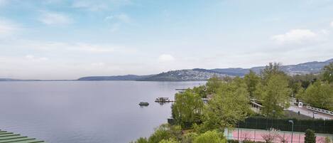 A view of a lake with boats, a tennis court, and a city in the distance.