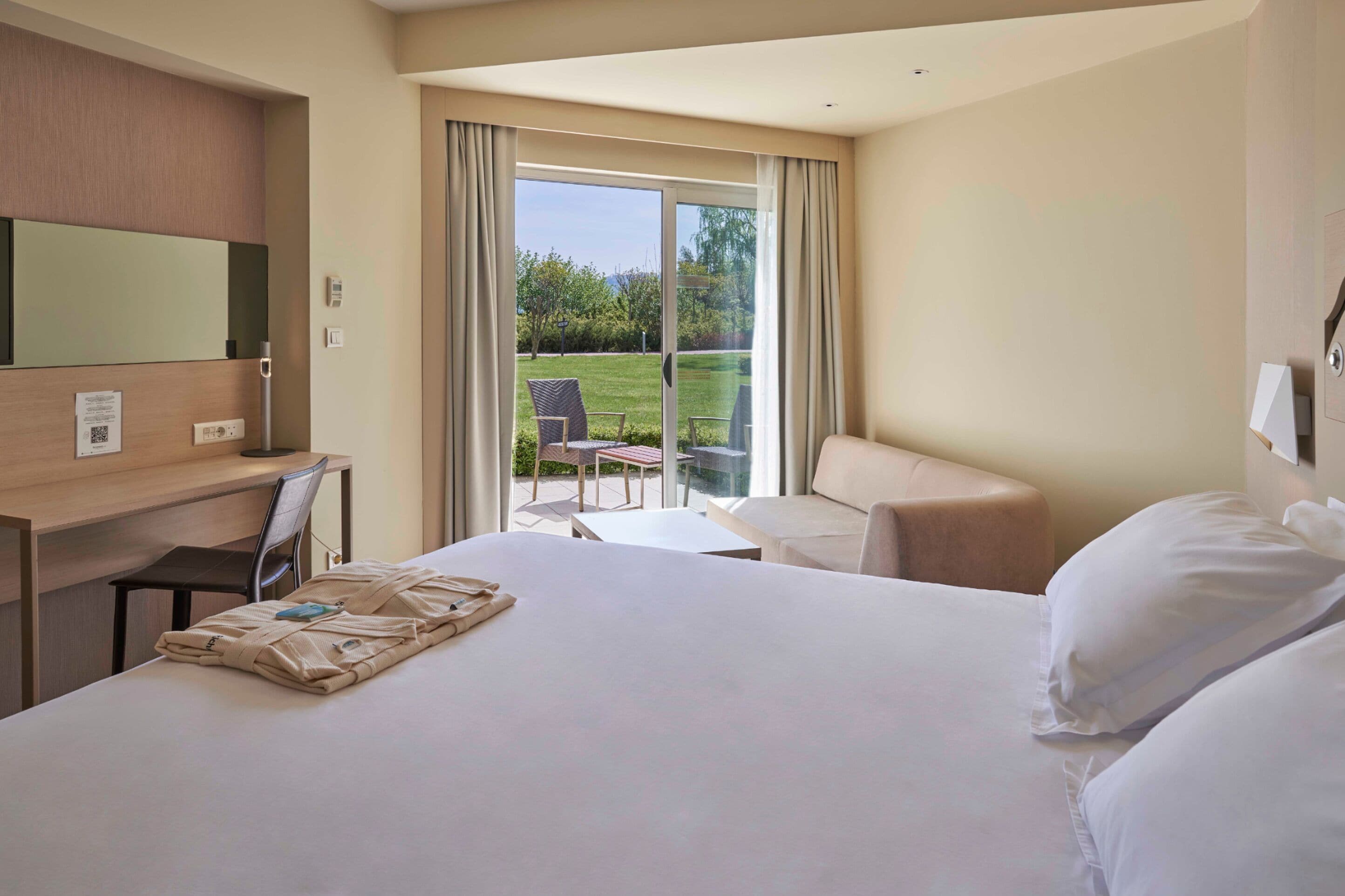 Une chambre d’hôtel avec un grand lit, un bureau, une chaise et une vue sur l’extérieur grâce à une porte-fenêtre coulissante.