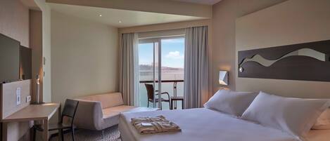 A hotel room with a large bed, a desk, a chair, and a balcony with a view.