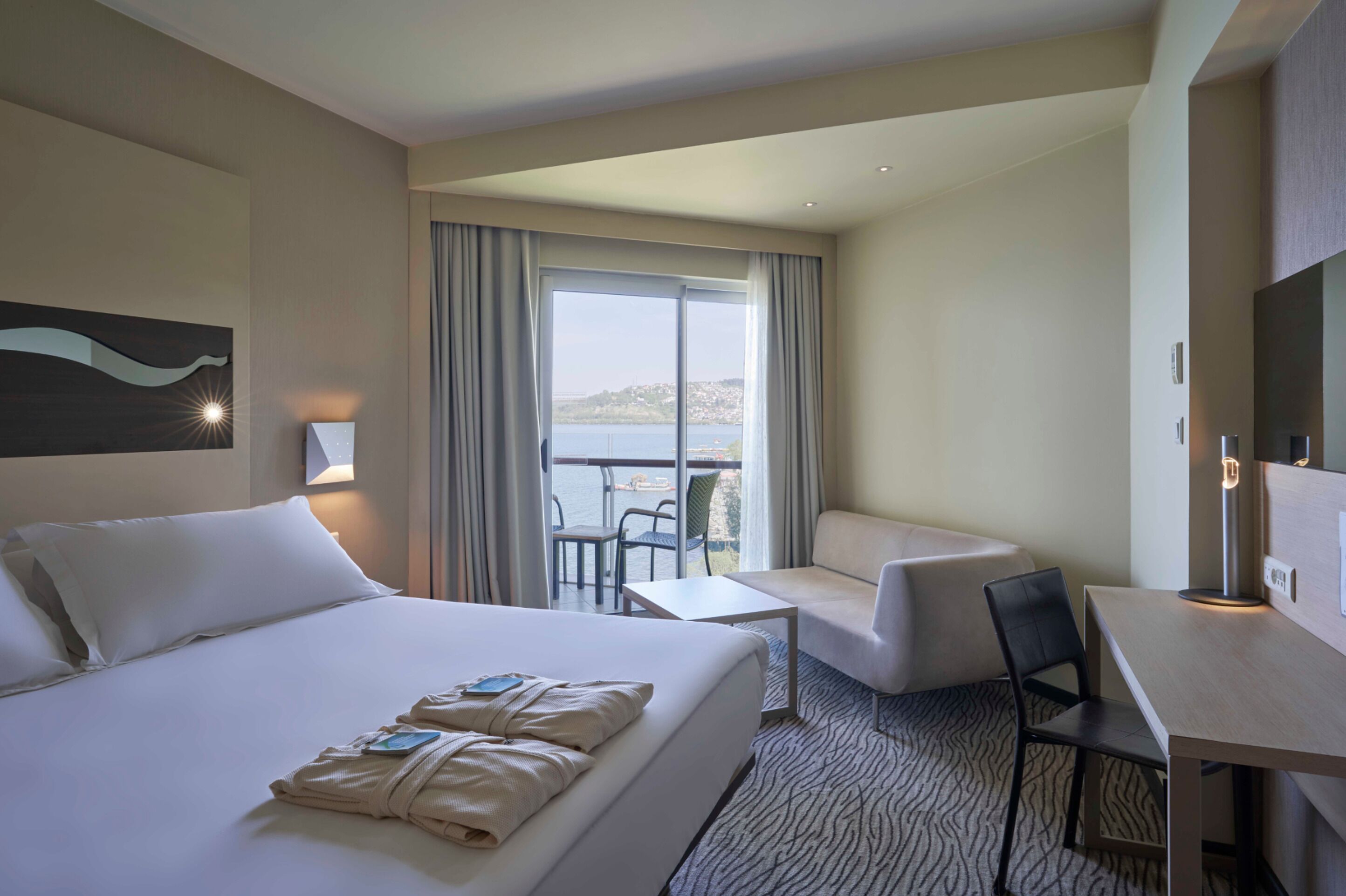 Une chambre d’hôtel avec un grand lit, un bureau, une chaise et un balcon donnant sur l’eau.