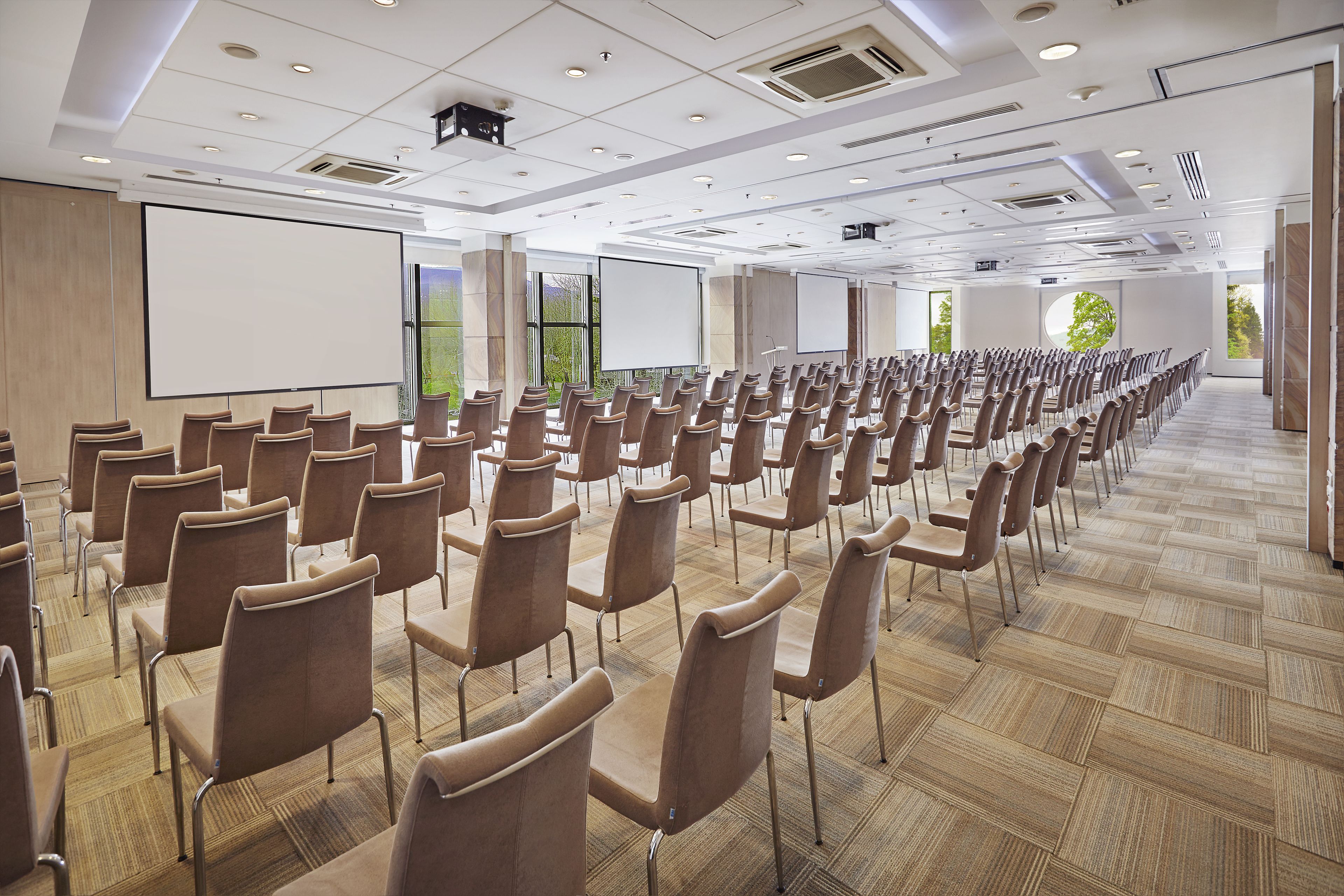 Un salón de conferencias con filas de sillas, una pantalla grande y un proyector.