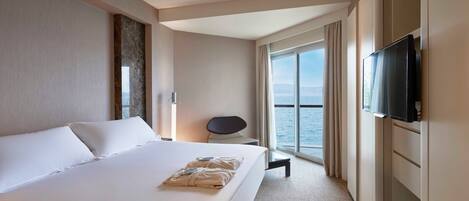 Habitación de hotel con una cama grande, un televisor de pantalla plana, una silla y vista al mar.