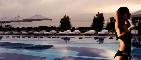 Una piscina al aire libre, sombrillas, sillones reclinables de piscina