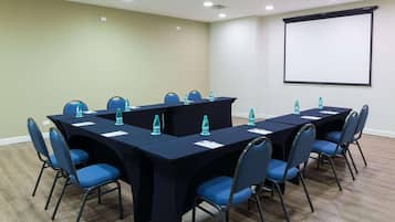 A conference room with a long table, chairs, water bottles, and a projector screen.