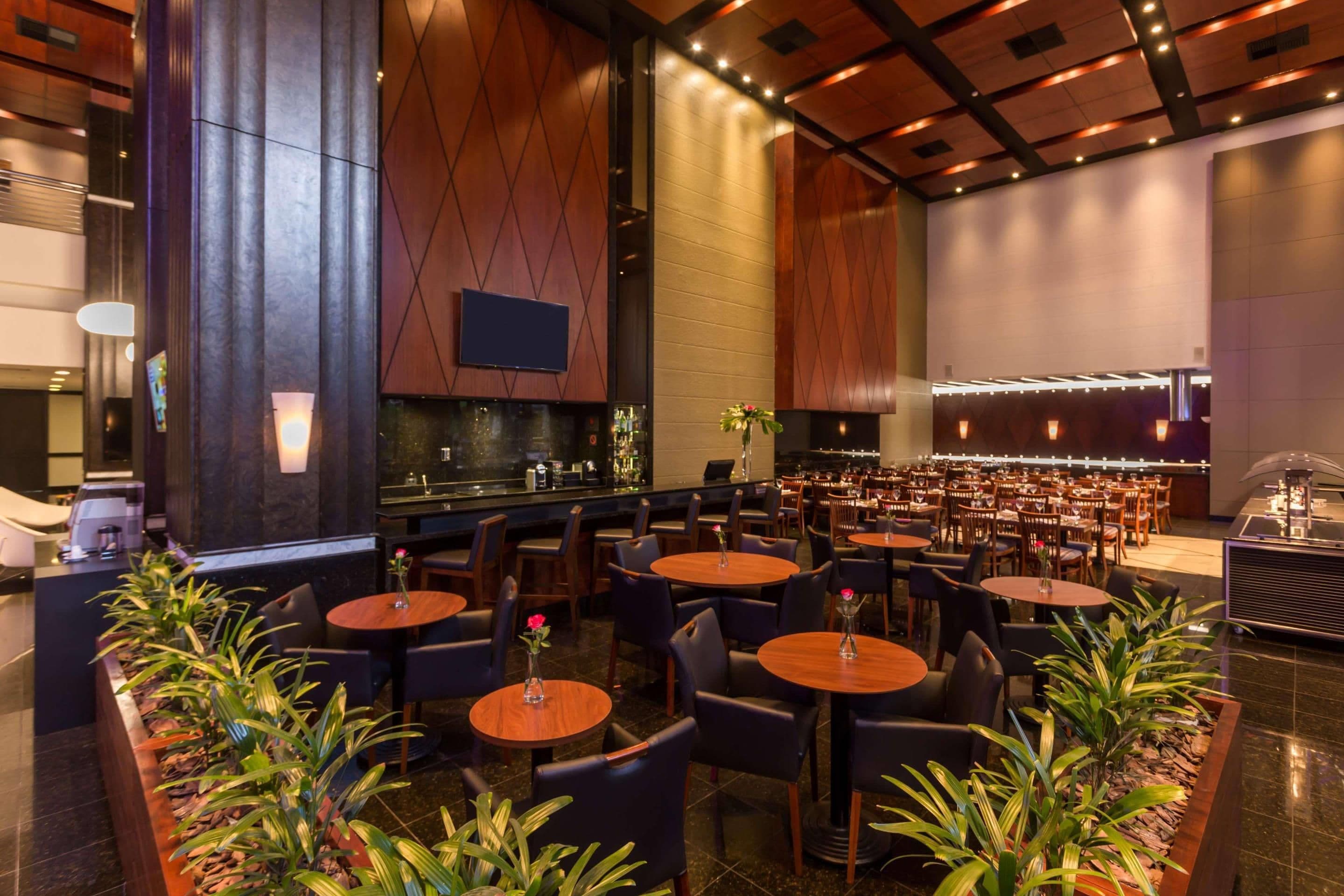 Un restaurant spacieux avec de nombreuses tables et chaises, un coin bar et un grand écran fixé au mur.