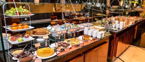 A buffet with various food items and beverages, including fruits, pastries, and hot drinks.