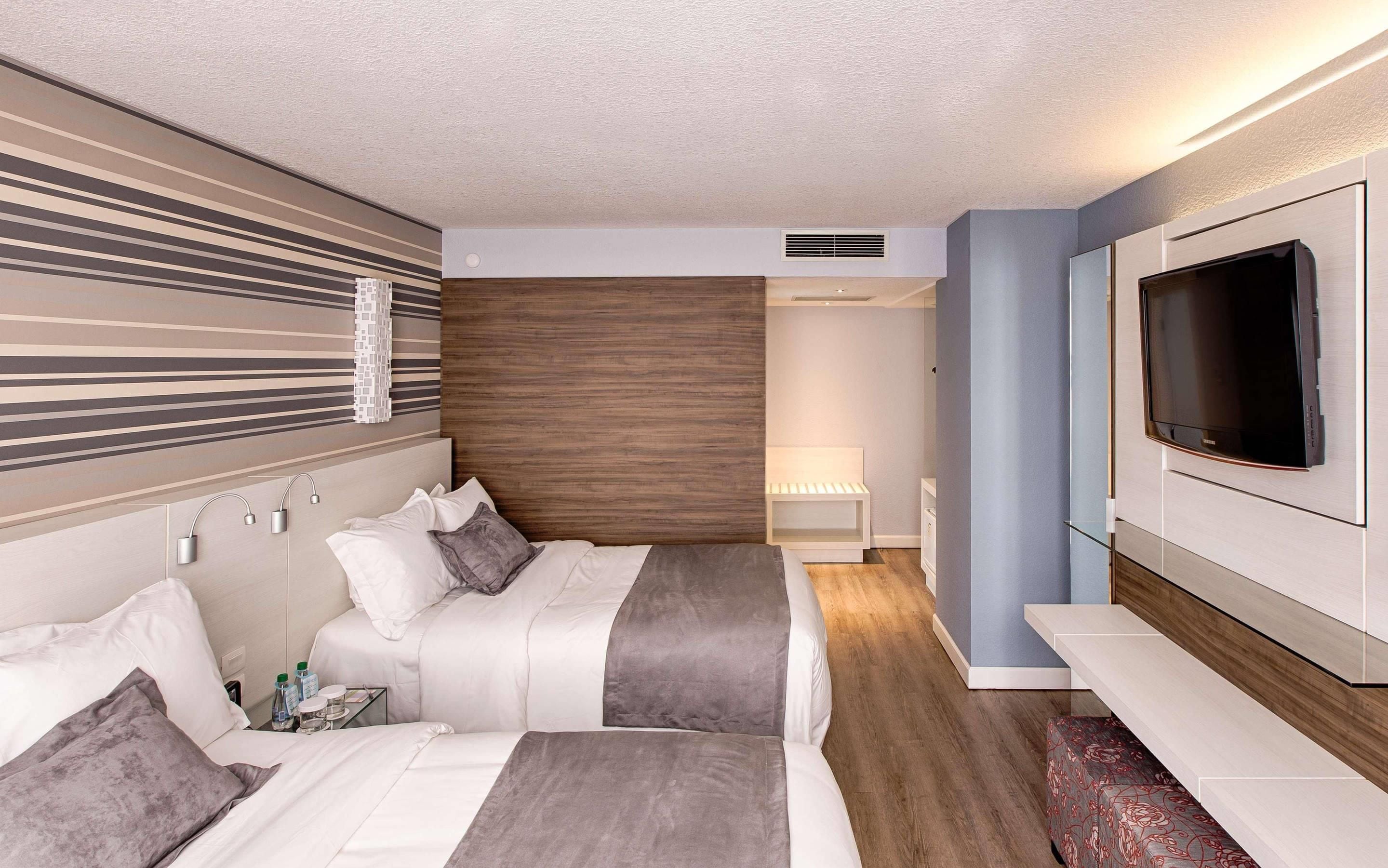Una habitación de hotel con una cama, mesitas de noche, un televisor y un baño al fondo.