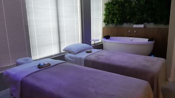 Relax in this serene spa room featuring a bathtub, massage beds, and a calming plant.