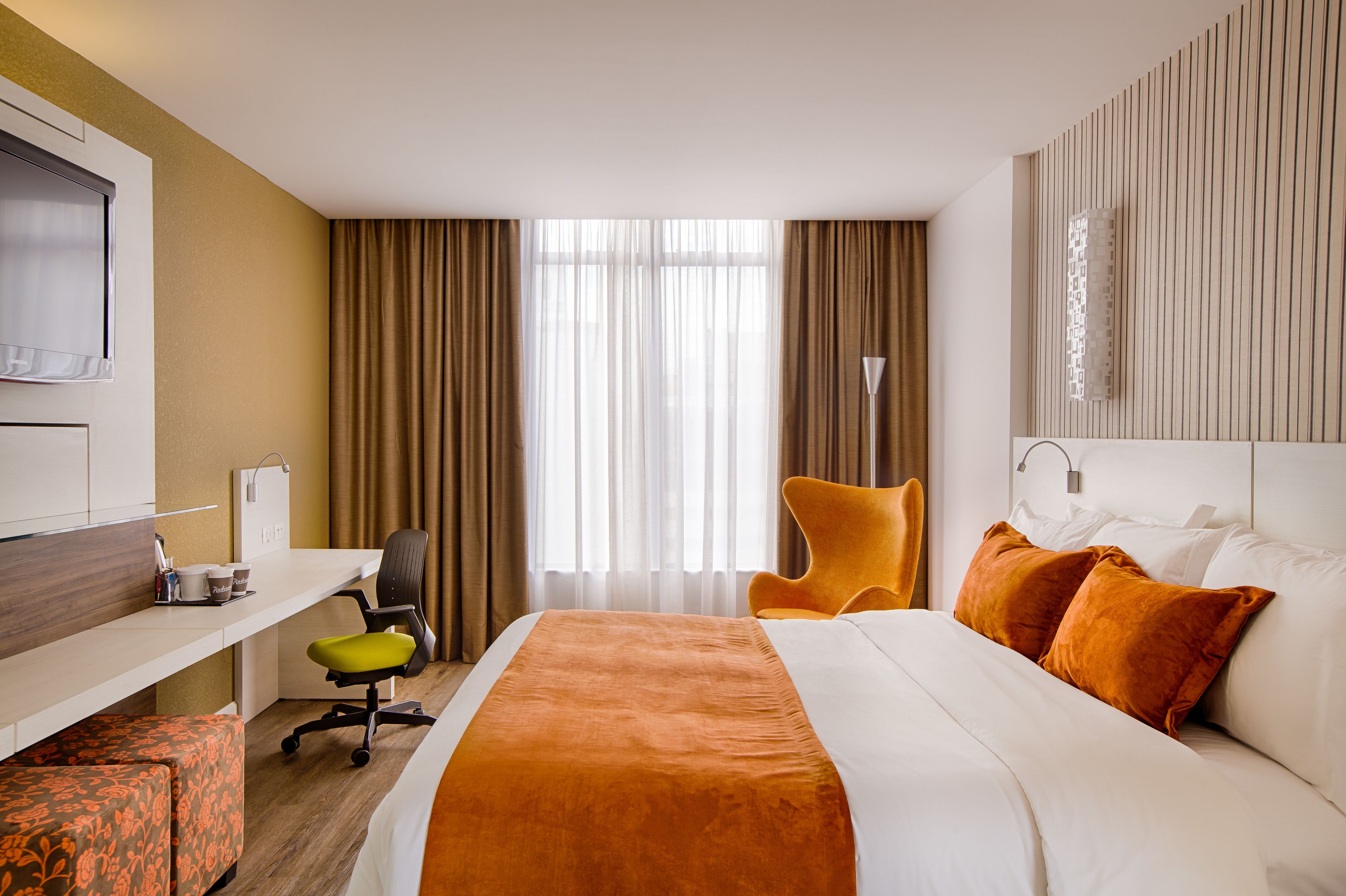 Una camera d'albergo con un letto, una scrivania, una sedia e un'ampia finestra con tende.