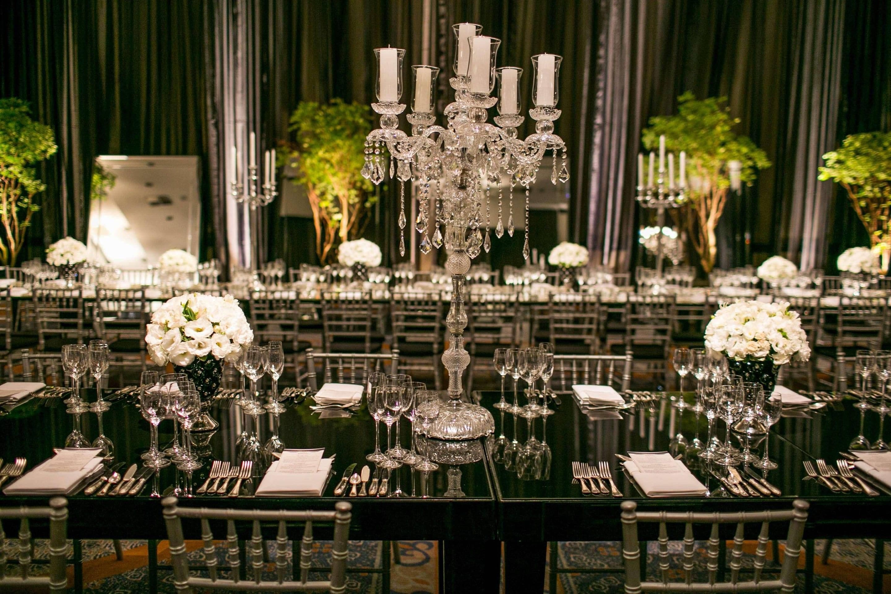 A formal dining setting with tables set for multiple guests, featuring crystal glassware, silverware, and white floral centerpieces.