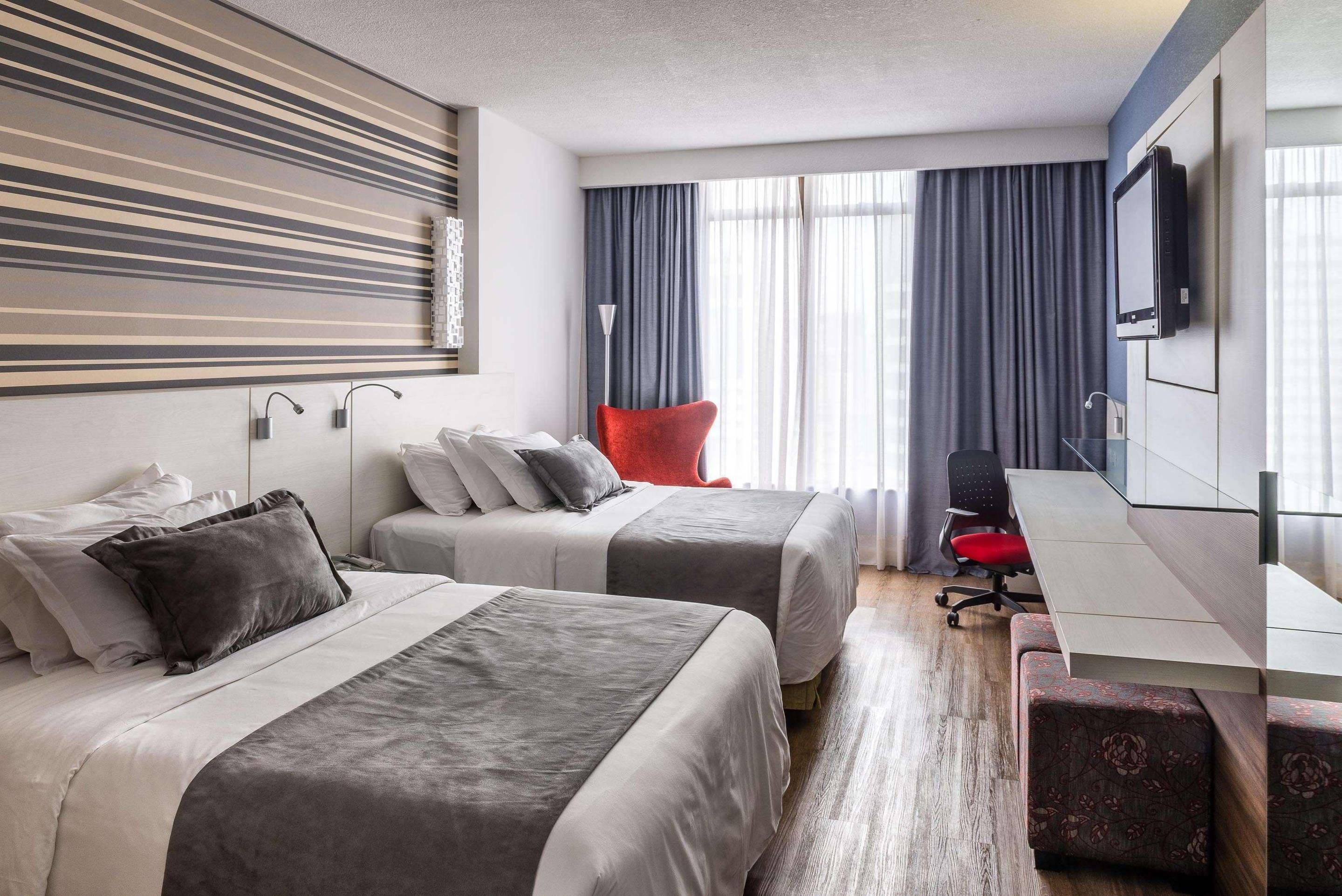 A hotel room with two beds, a desk, a chair, a TV, and a window with curtains.